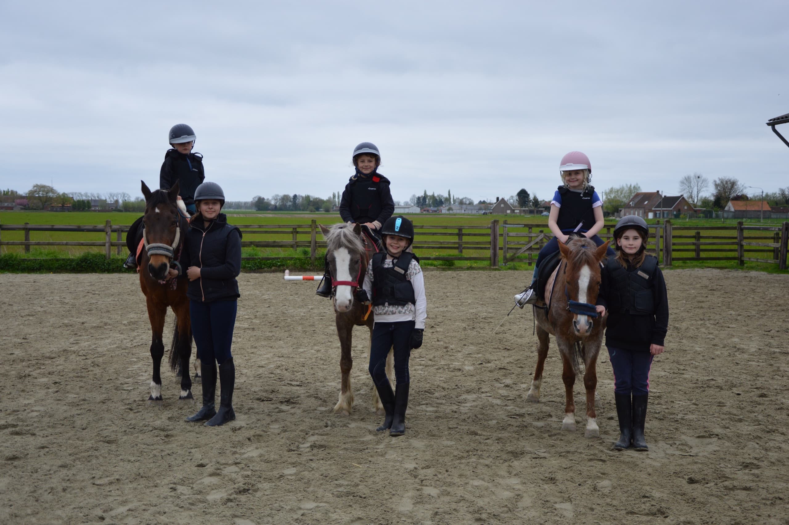 Jonge ruiters poseren met hun pony's en begeleiders op de buitenpiste bij Start 2 Pony