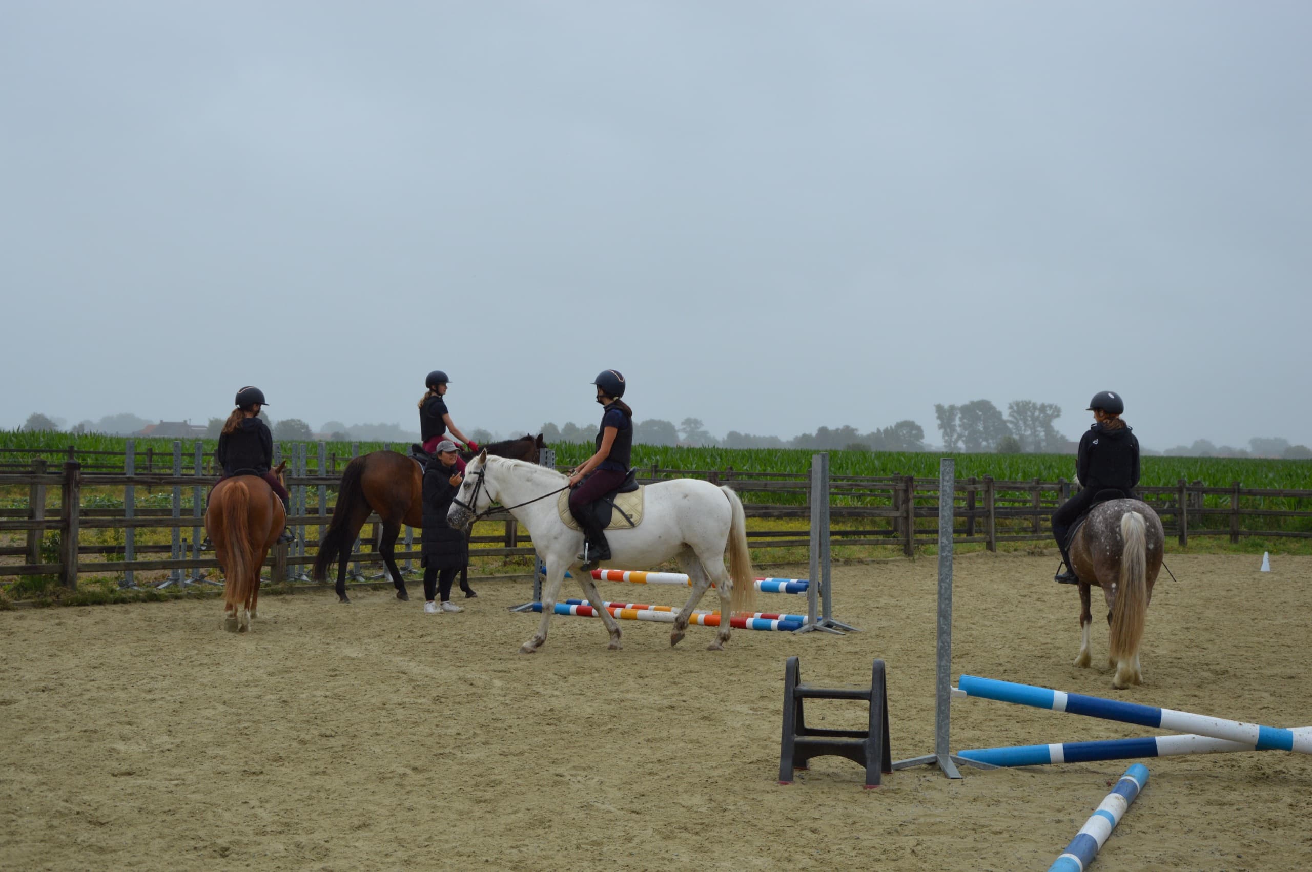 Ruiters wachten te paard tussen de hindernissen op de buitenpiste tijdens de bootcamp