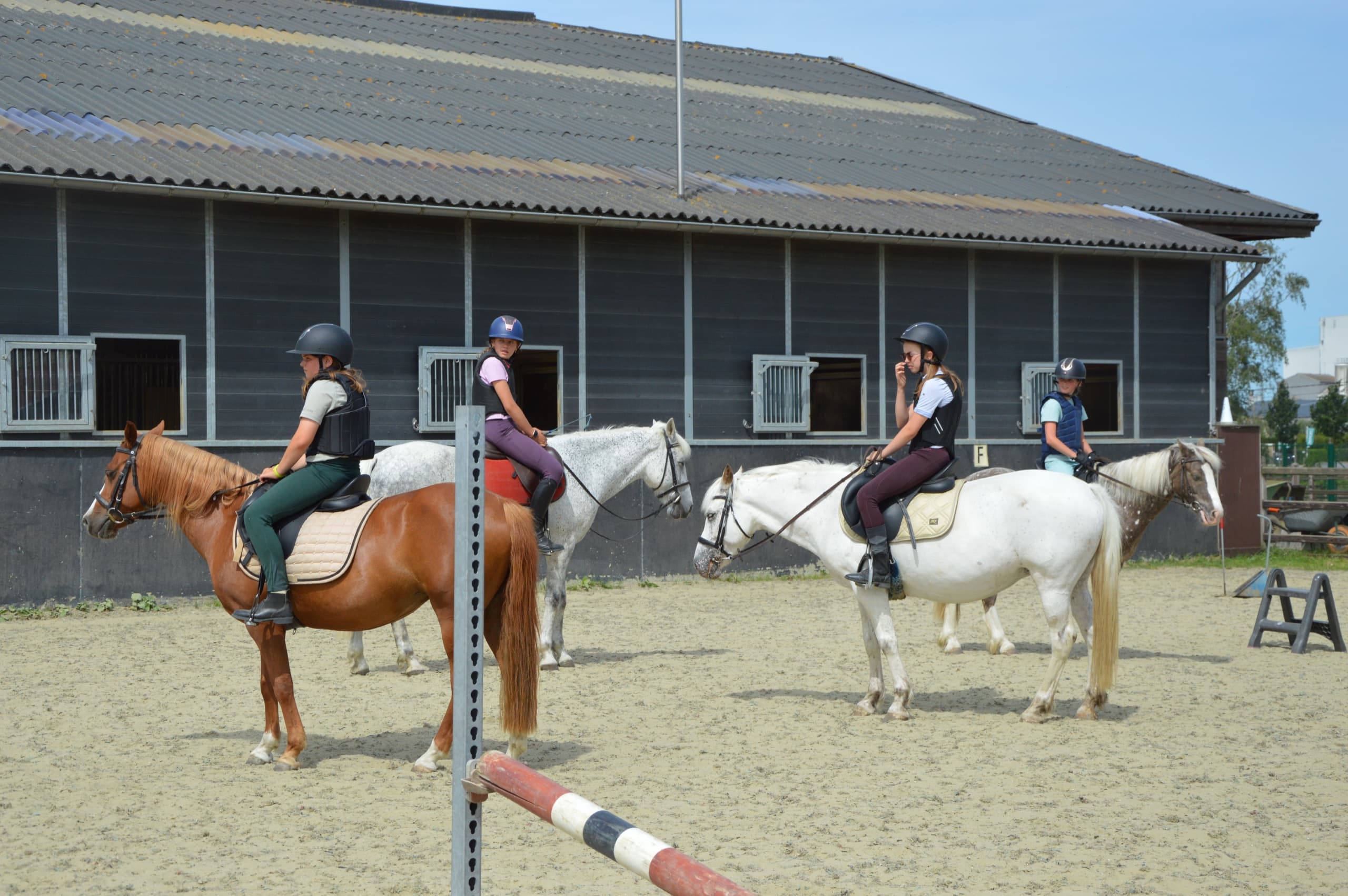 Vier ruiters op pony's naast elkaar op de buitenpiste voor de stallen